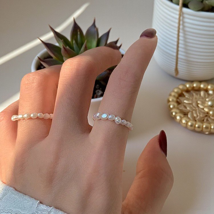 Hand wearing a pearl ring with a blurred background of plants and decor