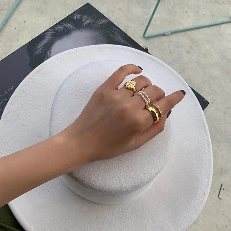 Hand wearing multiple gold rings on a white surface with a blurred background
